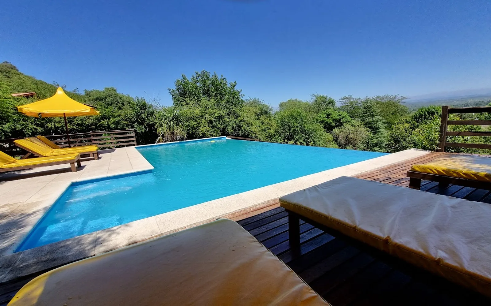 Pileta panorámica con deck, reposeras y sombrillas amarillas frente a las sierras